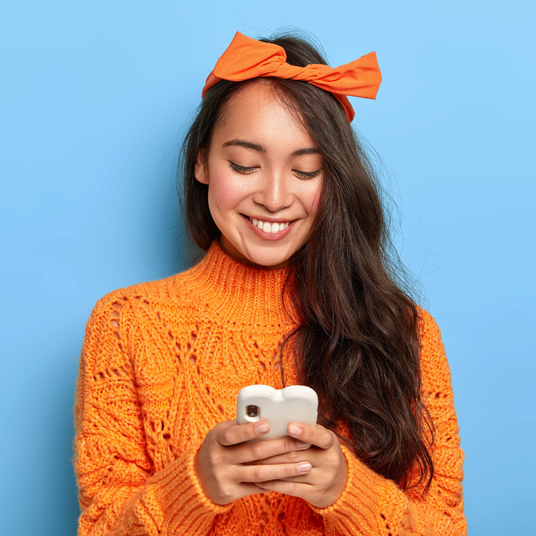 Jeune femme regardant son téléphone en souriant, fond bleu