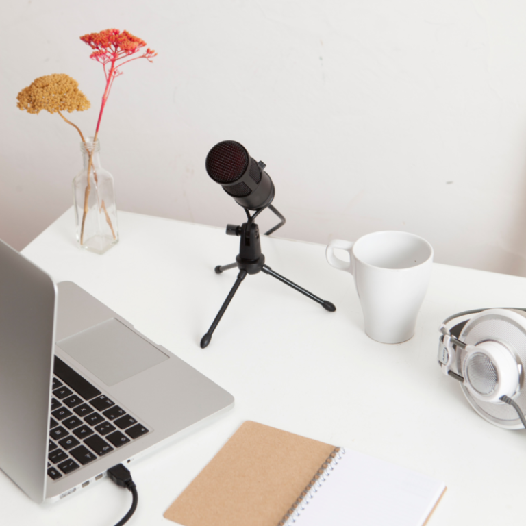 Photo d'un bureau avec ordinateur, carnet, micro, casque audio et tasse.